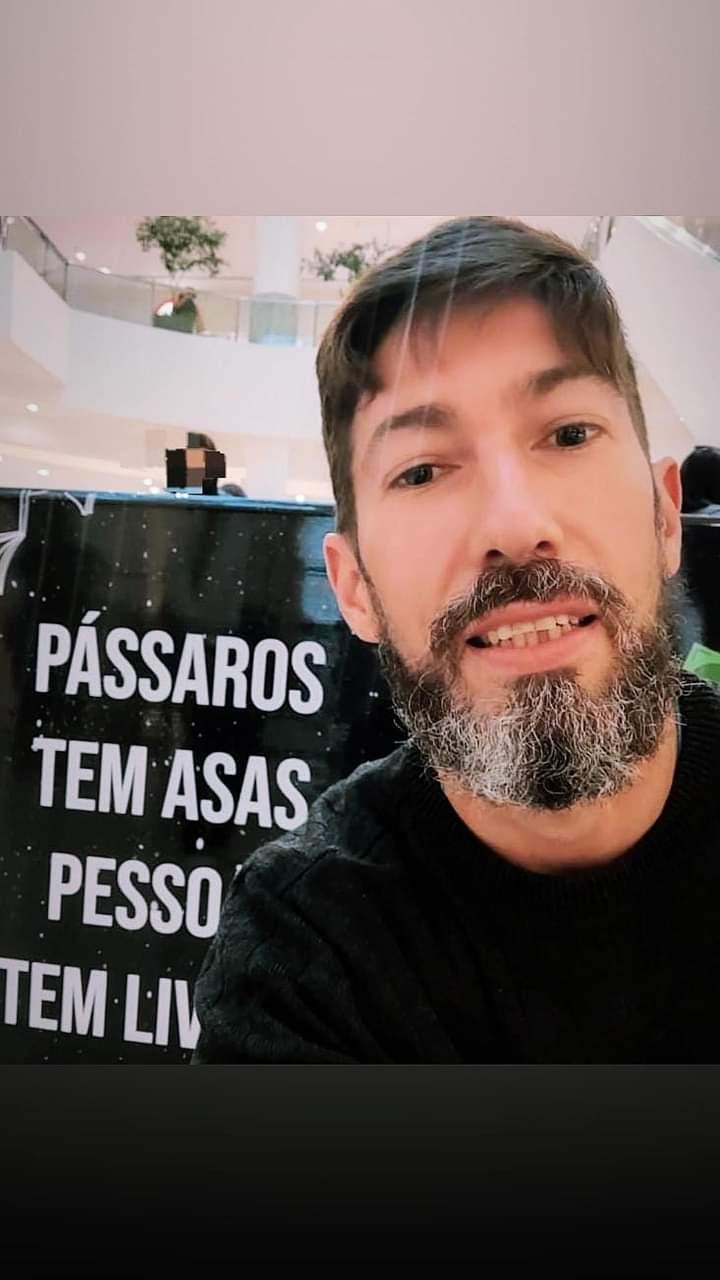 Rodrigo em evento cultural, ao lado da frase 'Pássaros têm asas, pessoas têm livros'